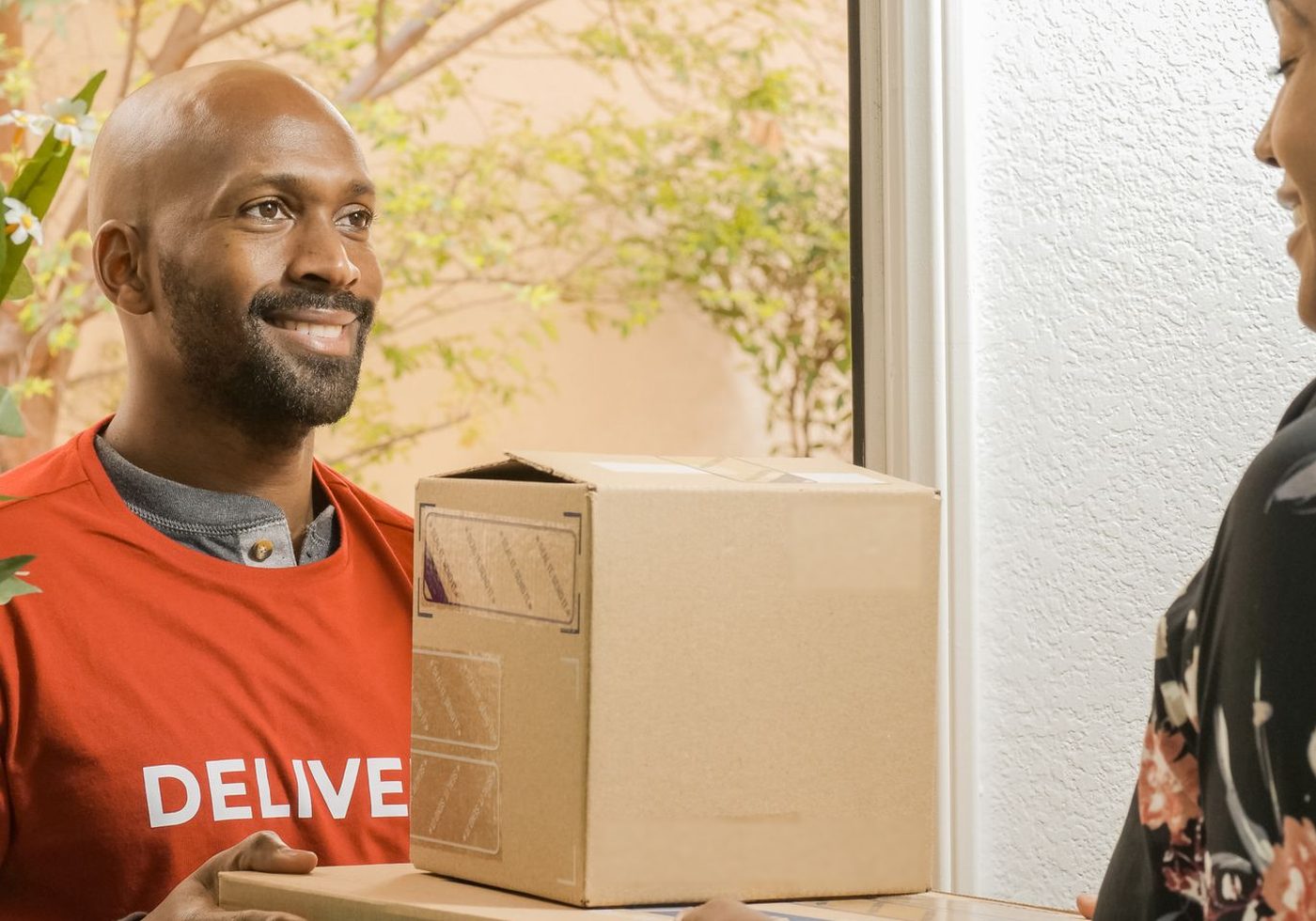 A smiling delivery man handing an order to a customer at her door